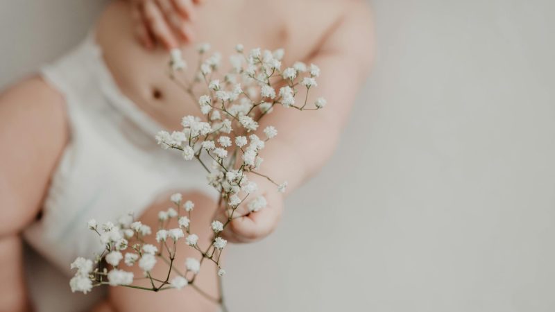Portrait of a baby in a diaper delicately holding white flowers, emphasizing innocence.